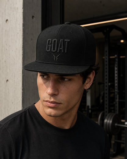 Gorra GOAT Total Black negra con bordado tonal, llevada por modelo en entorno de gimnasio