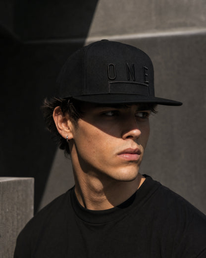 Gorra ONE Total Black negra con bordado tonal, llevada por modelo en entorno urbano