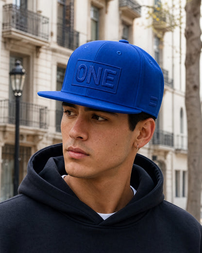 Gorra ONE Total Blue azul real con bordado tonal, llevada por modelo en ciudad